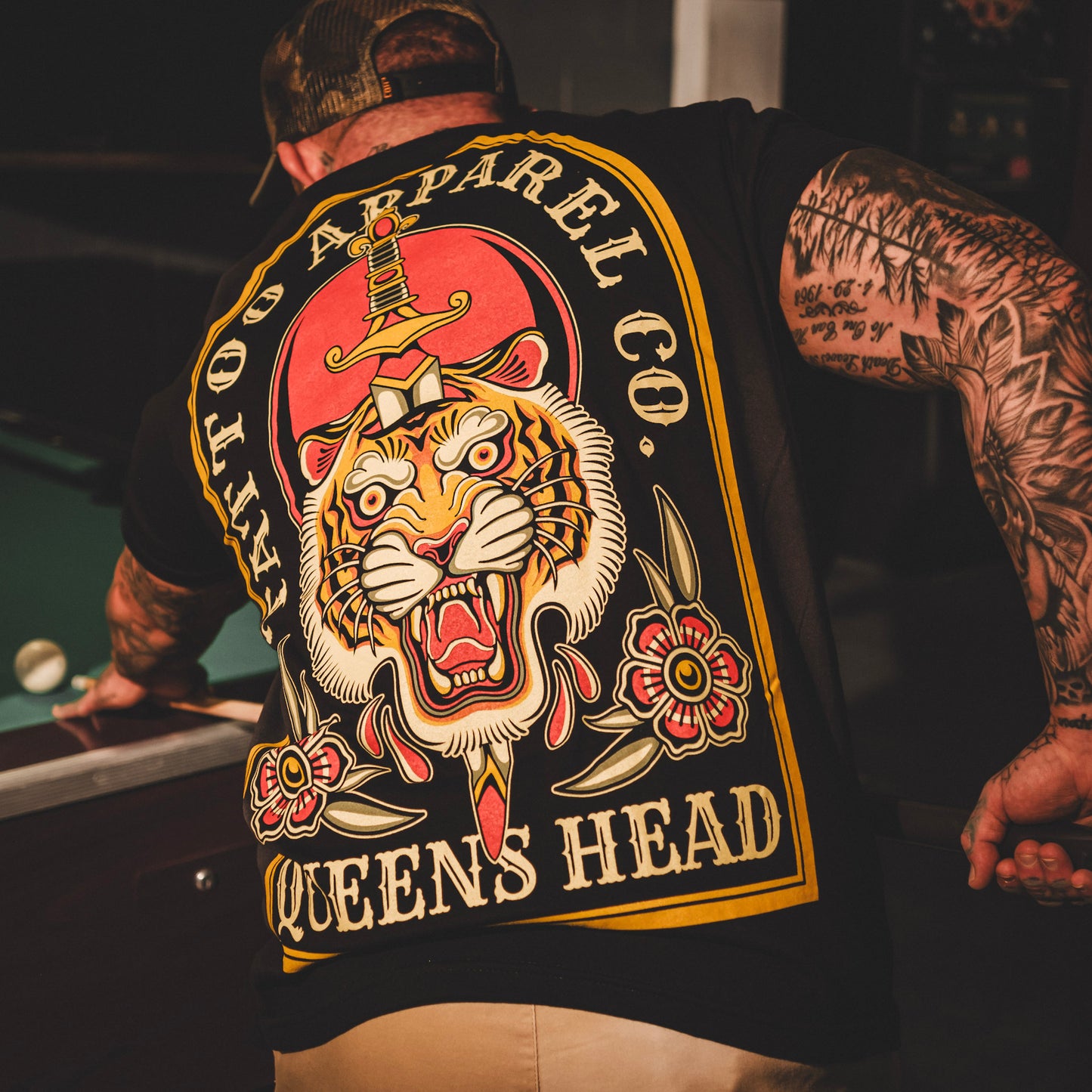 A person wearing a black T-shirt with a traditional tiger design, the shirt has the text QUEENS HEAD on it.