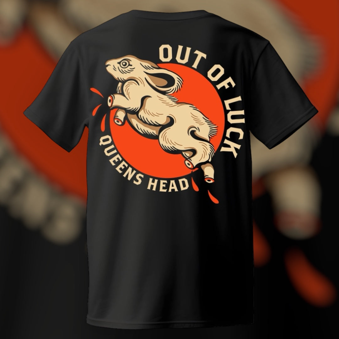 Black T-shirt with a front left chest graphic of a rabbit's foot keychain and a central graphic of a rabbit with missing feet running in a circle with the text 'OUT OF LUCK' and 'QUEENS HEAD'.